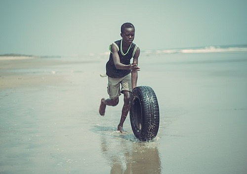 A child rolling a tire along a beach